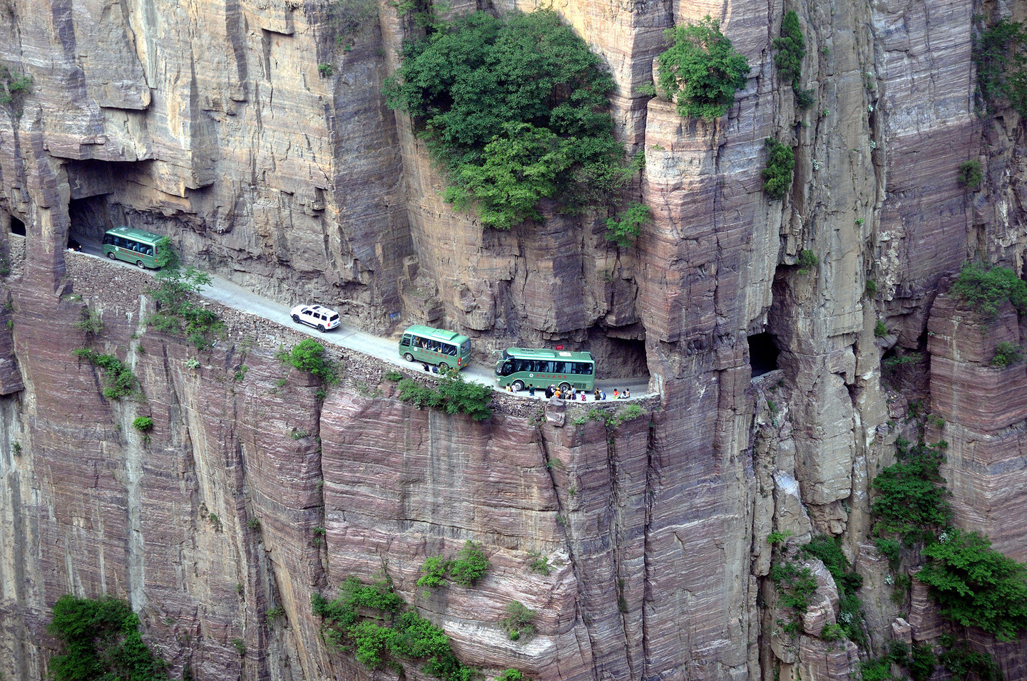 --FILE--Buses and cars travel along the Guoliang Tunnel through the Wanxian Mountain in the Taihang Mountains in Huixian county, Xinxiang city, central China's Henan province, 17 May 2014. The Guoliang Tunnel in Taihang Mountains was built by local villagers themselves, which is an inspiring story in itself. Before 1972, the path chiseled into the rock used to be the only access linking the Village of Guoliang with the outside world. Then the villagers decided to dig a tunnel through the rocky cliff. Led by Shen Mingxin, head of the village, they sold goats and herbs to buy hammers and steel tools. Thirteen strong villagers starte to work on the project. It took them five years to finish the 1,200-meter-long tunnel which is about 5 meters high and 4 meters wide. Some of the villagers even gave their lives to it. On May 1, 1977, the tunnel was opened to traffic. The wall of the tunnel is uneven and there are more than 30 "windows" of different sizes and shapes. Some windows are round and some are square, and they range from dozens of meters long to standard-window-size. It is frightening to look down from the windows, where strange rocks hanging form the sheer cliff above and a seemingly bottomless pit lying below.