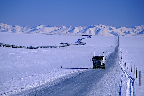 Alaska. Dalton Highway. Arctic winter. Trans Alaska Pipeline snakes across the tundra next to a truck driving on the highway hauling freight.